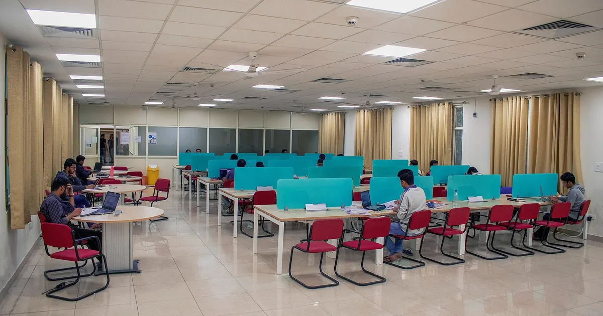 Students working at desks with laptops in a bright library reading hall