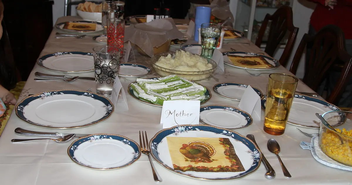 A Thanksgiving table set with blue-rimmed plates, place cards and a turkey-print napkin
